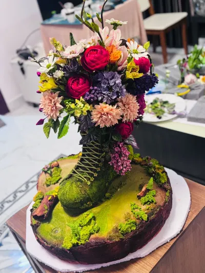 An award-winning hyper-realistic sugar art sculpture titled The Forgotten Step at FHAM 2024, featuring a moss-covered leather boot structure spilling over with hand-sculpted sugar flowers, peonies, and wild berries on an organic mossy base.
