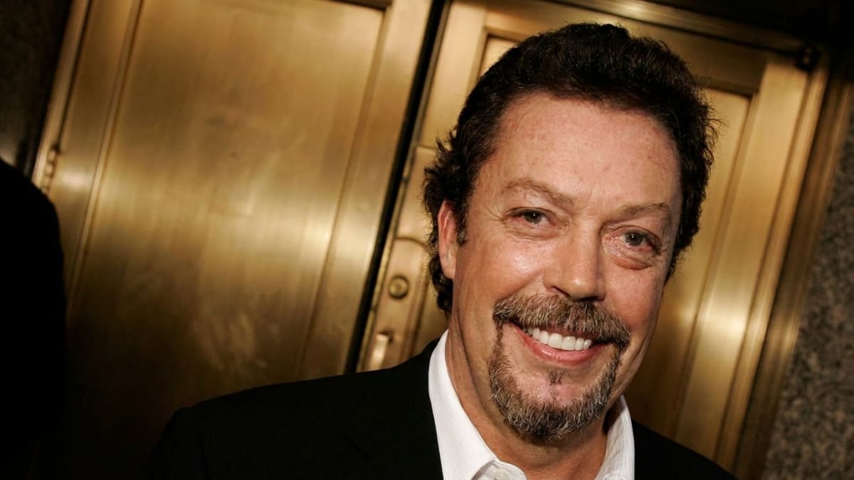 Tim Curry smiling in a black suit