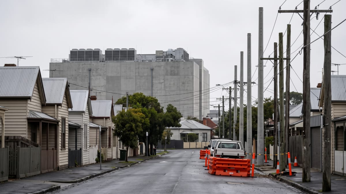 New concrete power poles and roadworks barriers on a residential street in Melbourne's inner west, with a data centre behind