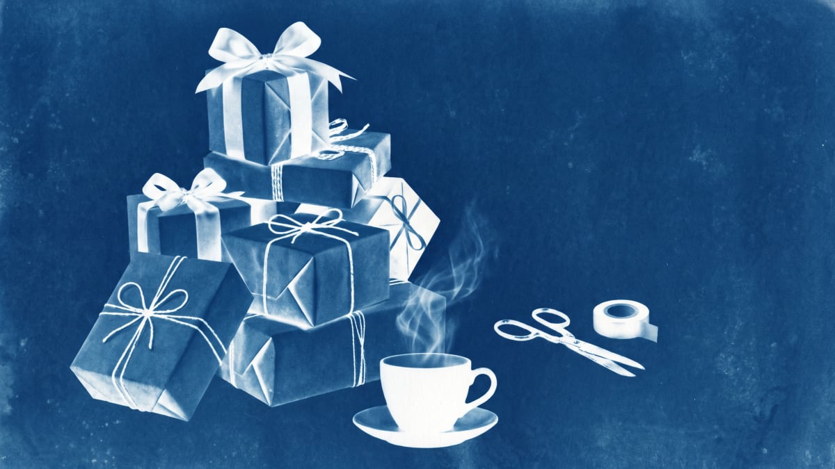 Cyanotype of a stack of wrapped presents, scissors and tape beside a steaming cup of tea