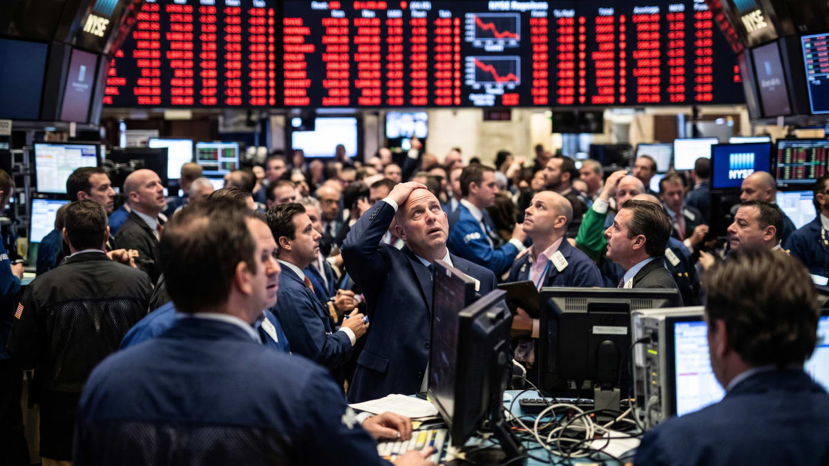 Traders on the New York Stock Exchange floor look up at screens showing falling prices