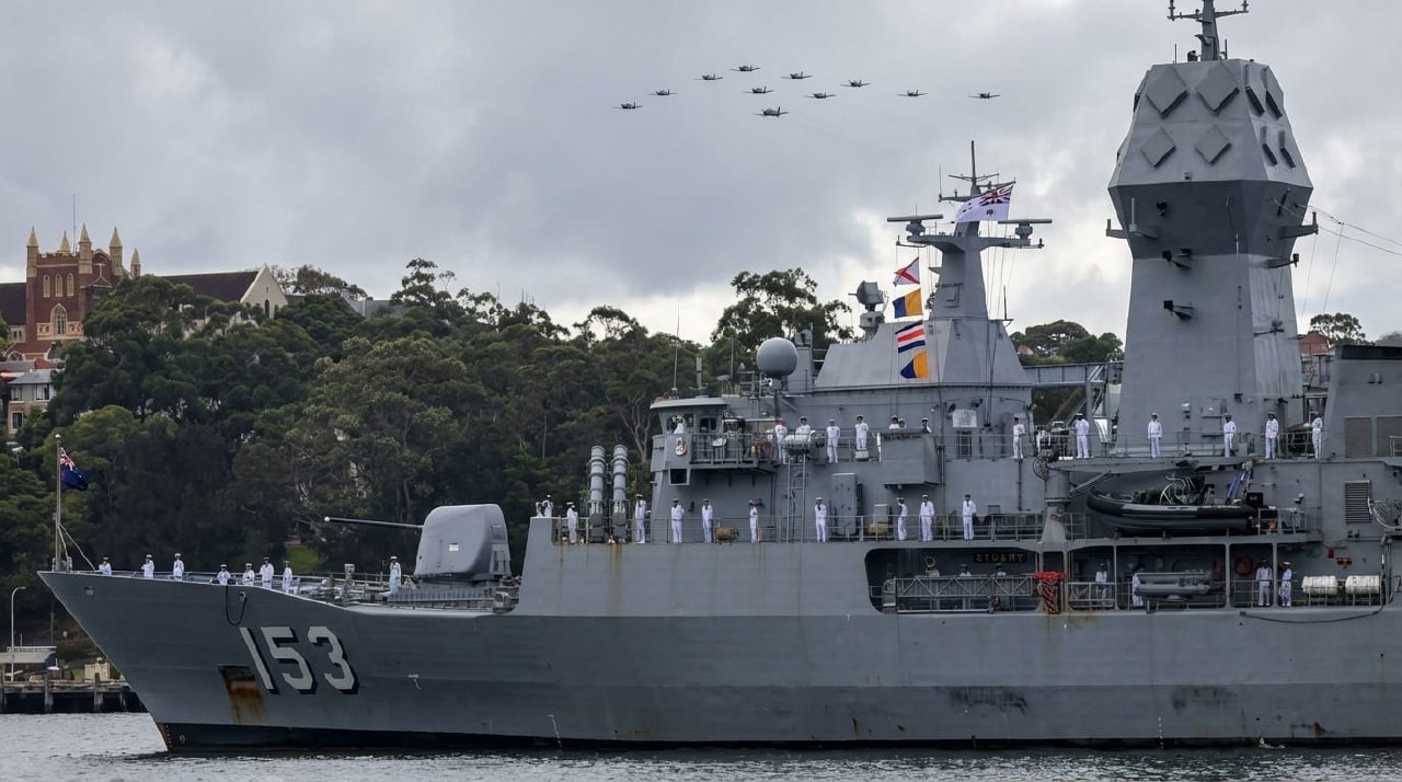 HMAS Stuart (FFH 153) with crew in dress whites as helicopters fly in formation overhead during Exercise Kakadu Fleet Review 2026