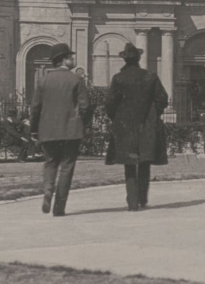Detail from the plate: two men from behind on the gravel path, one in a bowler, one in a long overcoat and soft felt hat