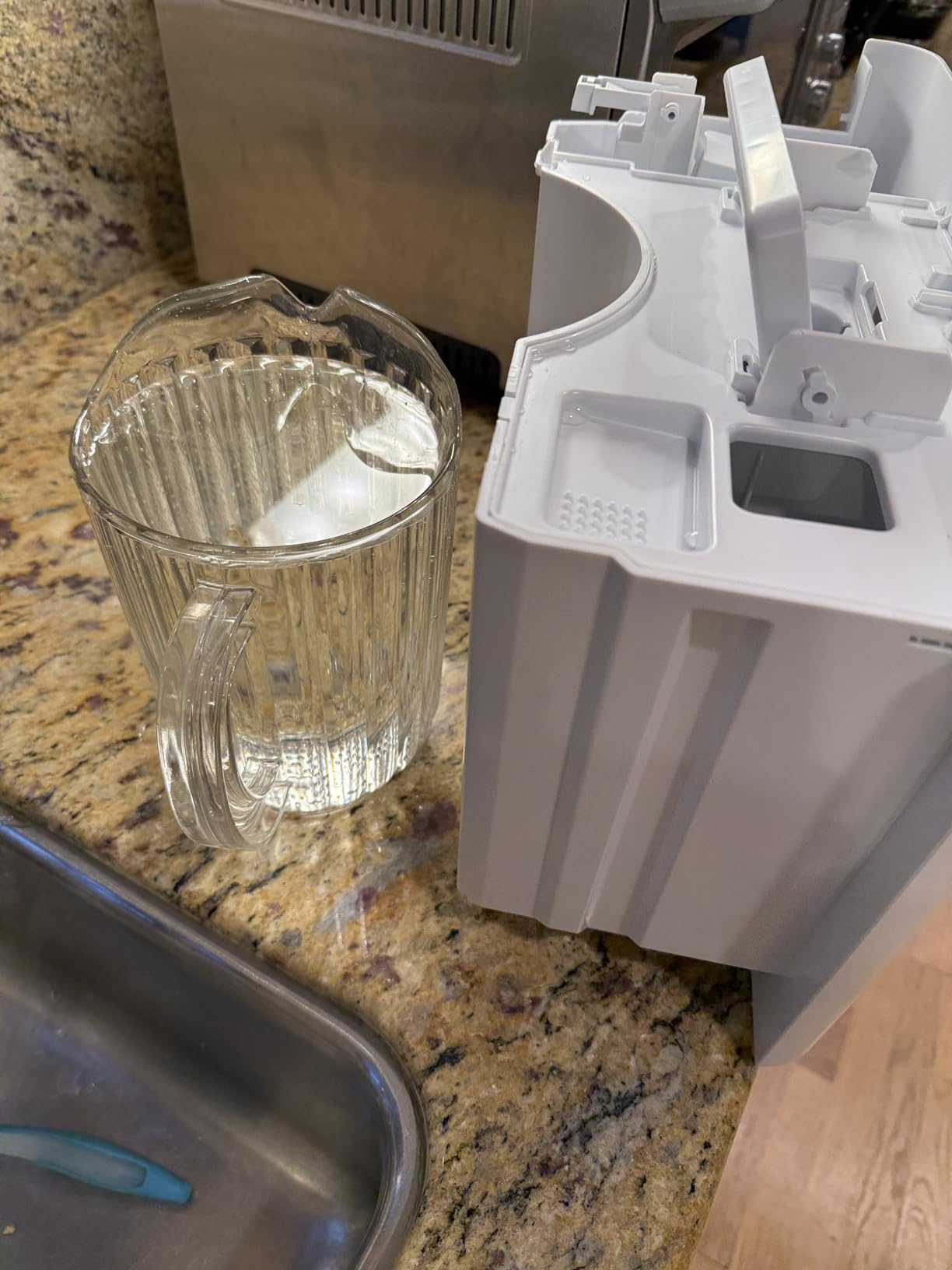 Clear glass pitcher next to the white GE dehumidifier water bucket with a carrying handle for capacity comparison