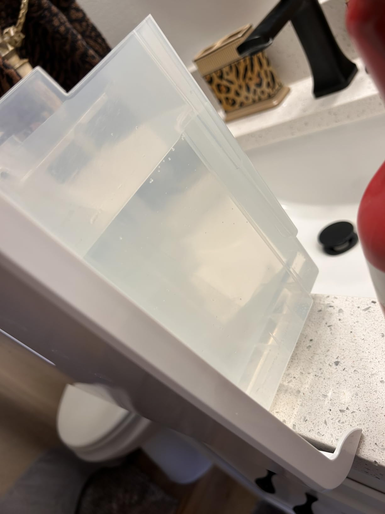 Translucent plastic water tank of the hOmeLabs dehumidifier filled with collected water, placed on a vanity near a bathroom sink