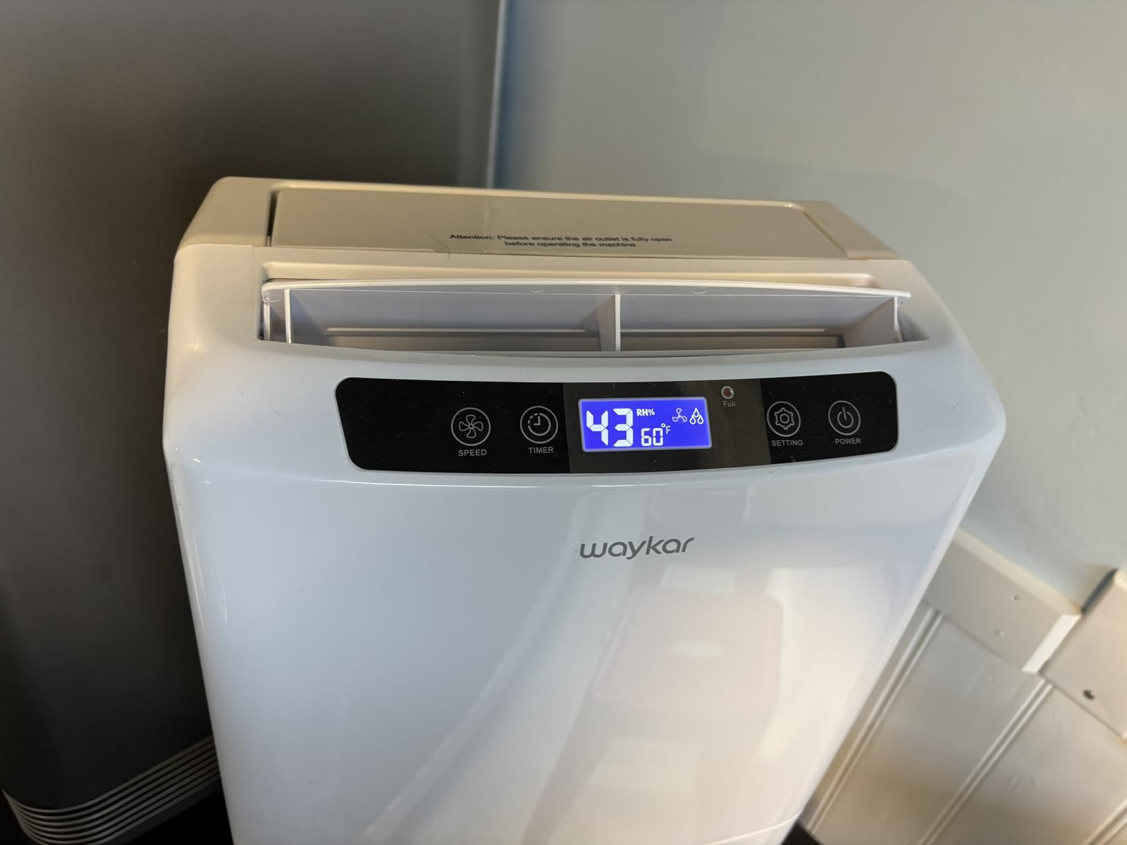 Close-up of the Waykar dehumidifier's control panel with a blue backlit display showing 43% relative humidity and 60 degrees F