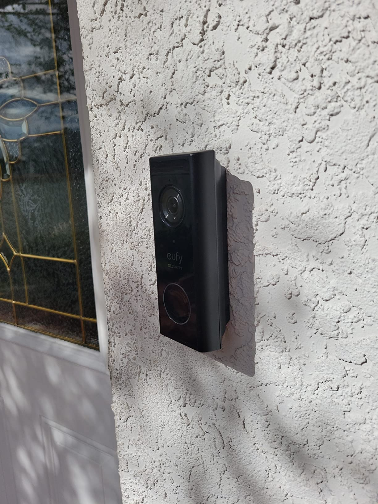 eufy Security Video Doorbell S220 mounted on a white stucco exterior wall next to the front door