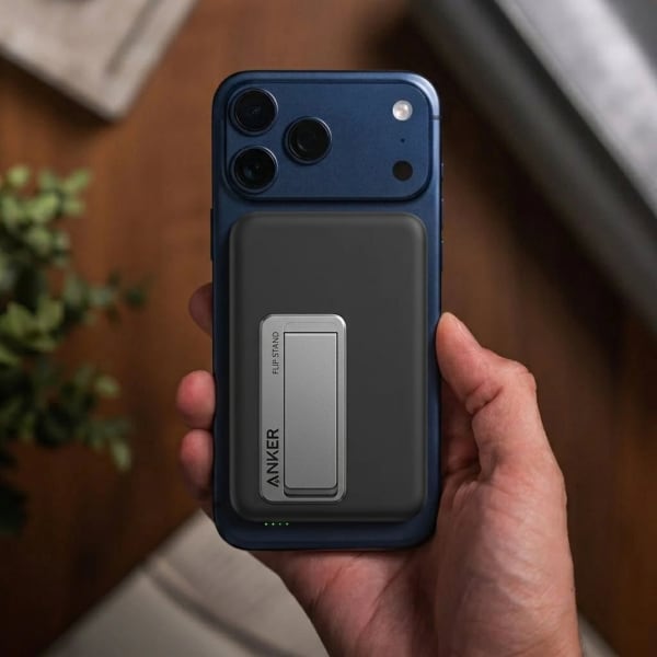 A sleek modern Qi2 magnetic wireless power bank attached to the back of a smartphone charging on a tabletop