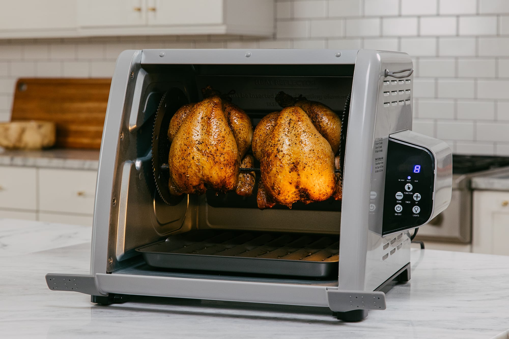 A beautifully roasted rotisserie chicken turning inside a countertop oven with glowing heating elements