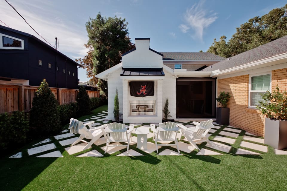 Backyard seating area with white Adirondack chairs, concrete pavers, turf, and an outdoor fireplace.