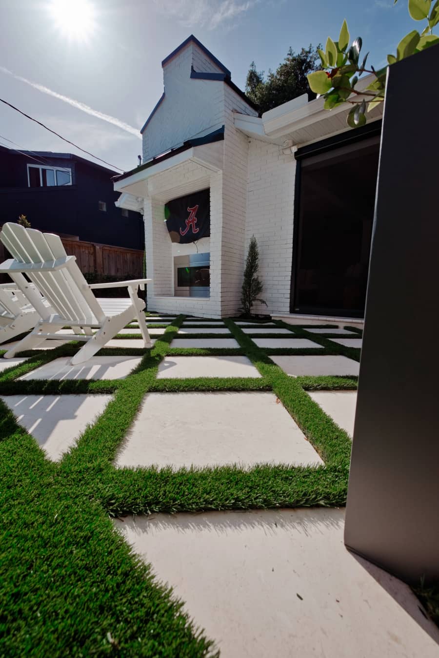 Low-angle view of concrete pavers with turf joints beside white Adirondack chairs and an outdoor fireplace.