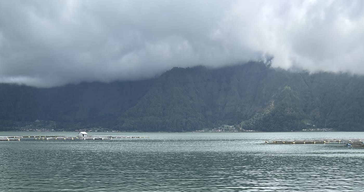 Cloud-covered mountains rising above a peaceful lake in Bali's volcanic highlands