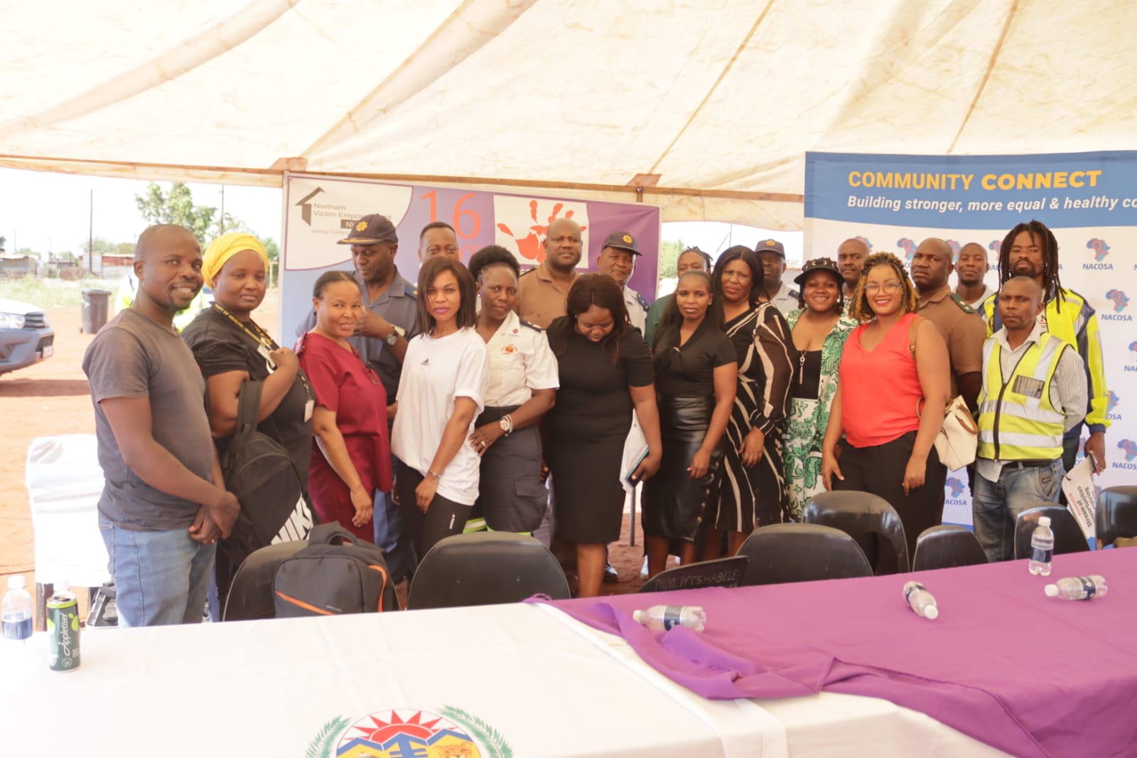 Staff, police officers and partners standing together at an activism campaign event with awareness banners behind them.