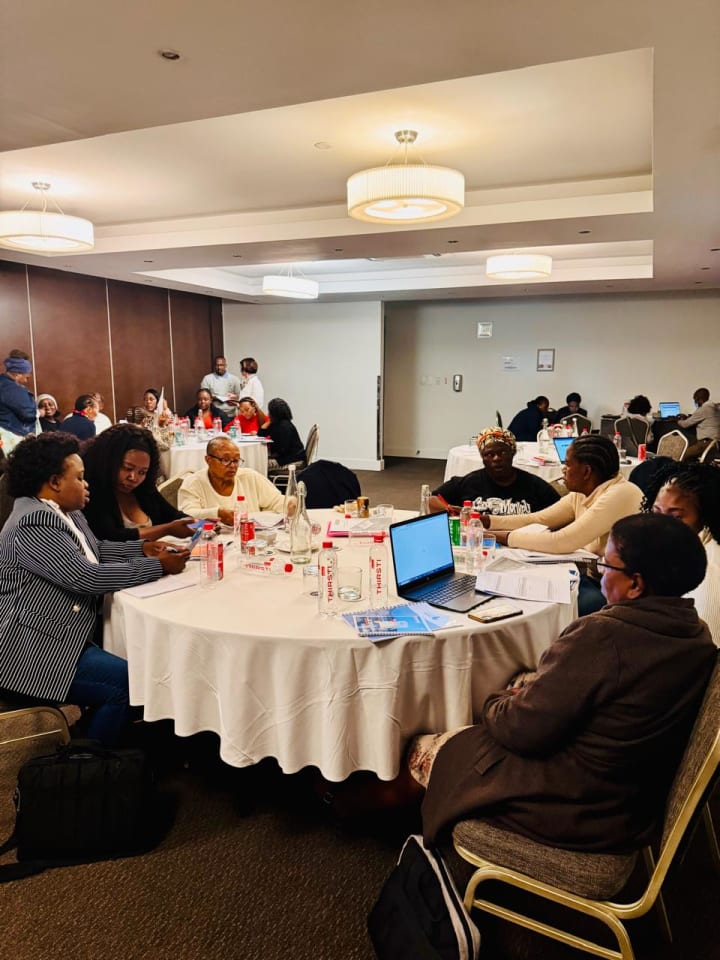 Participants seated around round tables during a training workshop, working with documents and a laptop.