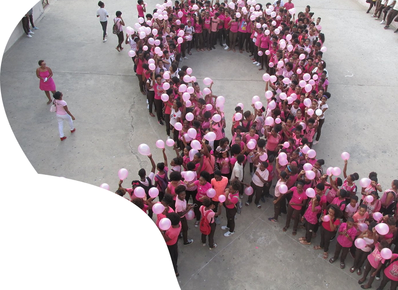 Grupo de estudantes em evento escolar, vestindo rosa e segurando balões para conscientização.