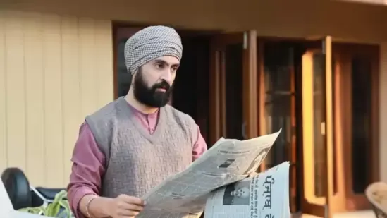 Bearded man wearing a grey turban and knitted vest reading a newspaper outside a house in a still from the Punjabi film Punjab 95.