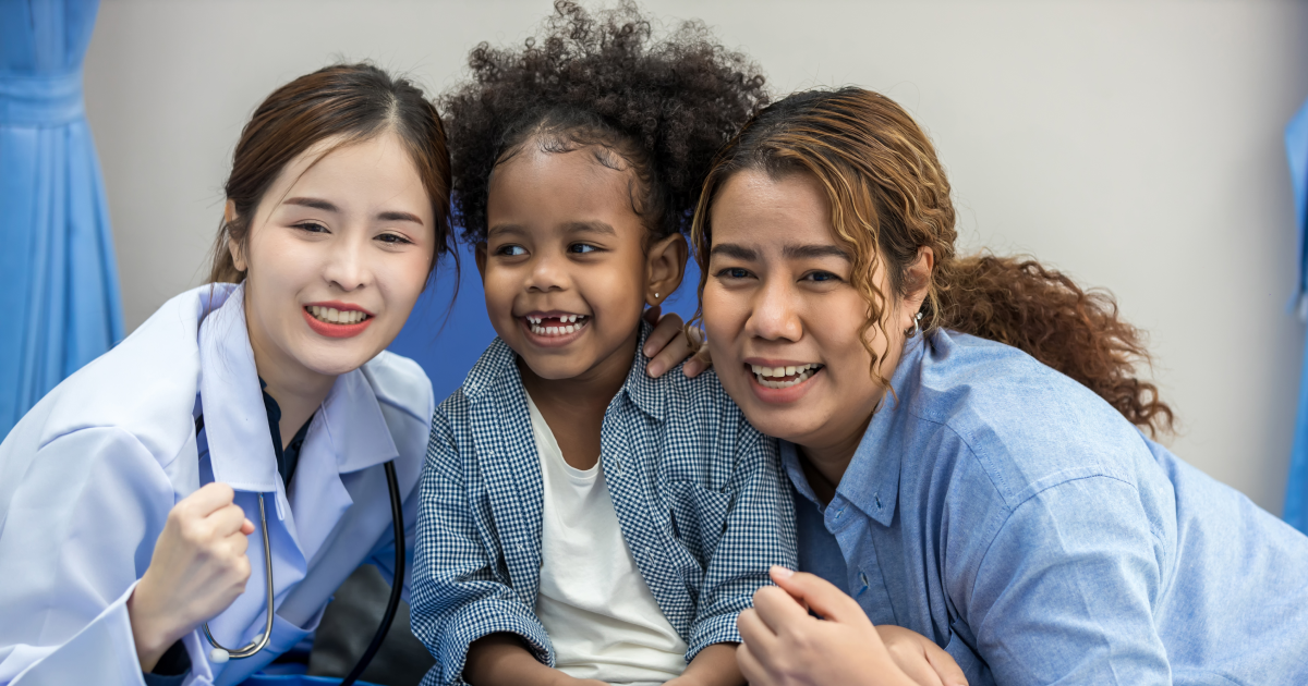 Smiling pediatrician posing with a laughing young child and parent in a medical setting