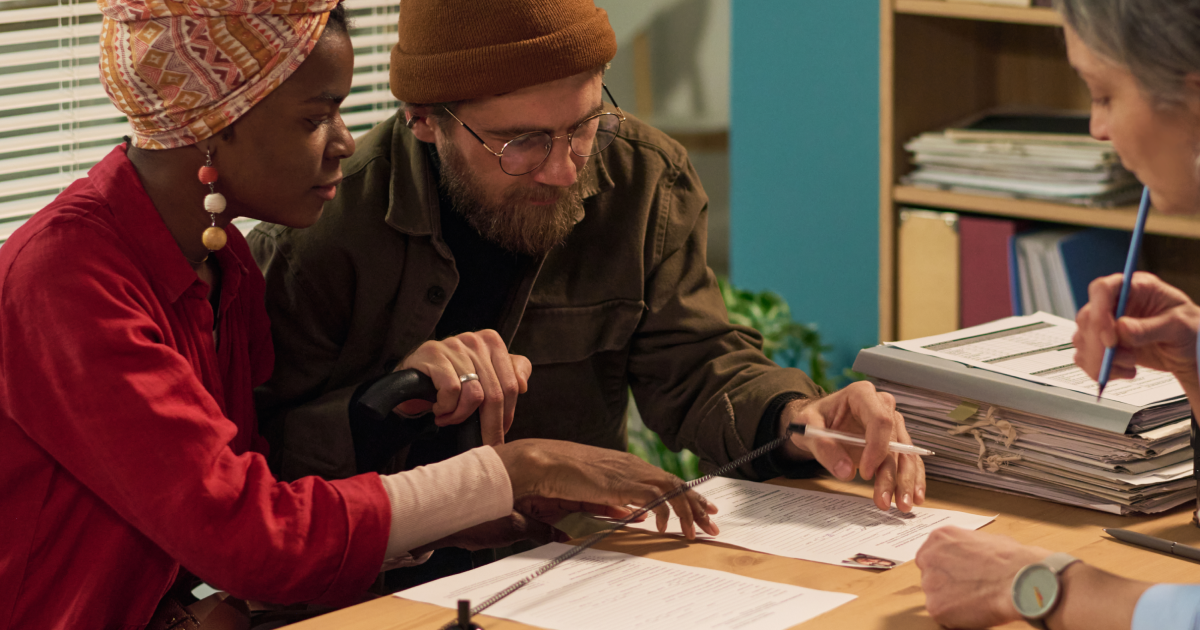 Couple leaning over paperwork at a desk while a professional takes notes in an office setting