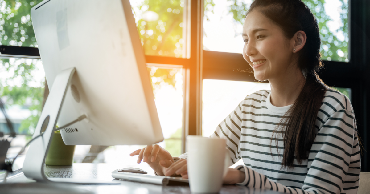 Young woman smiling while working at a desktop computer in a bright plant-filled workspace