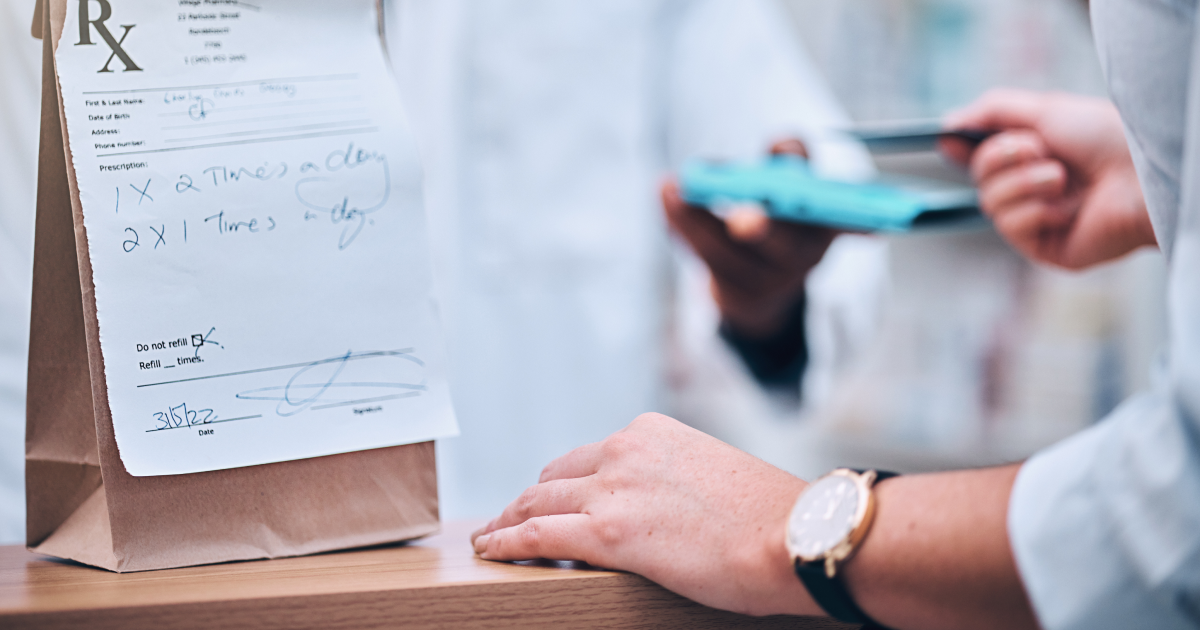 Pharmacy prescription bag with a handwritten medication label on a counter with a person holding a credit card