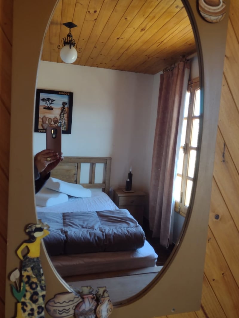 Perspectiva del dormitorio matrimonial con cama doble, luz natural matinal y espejo decorativo