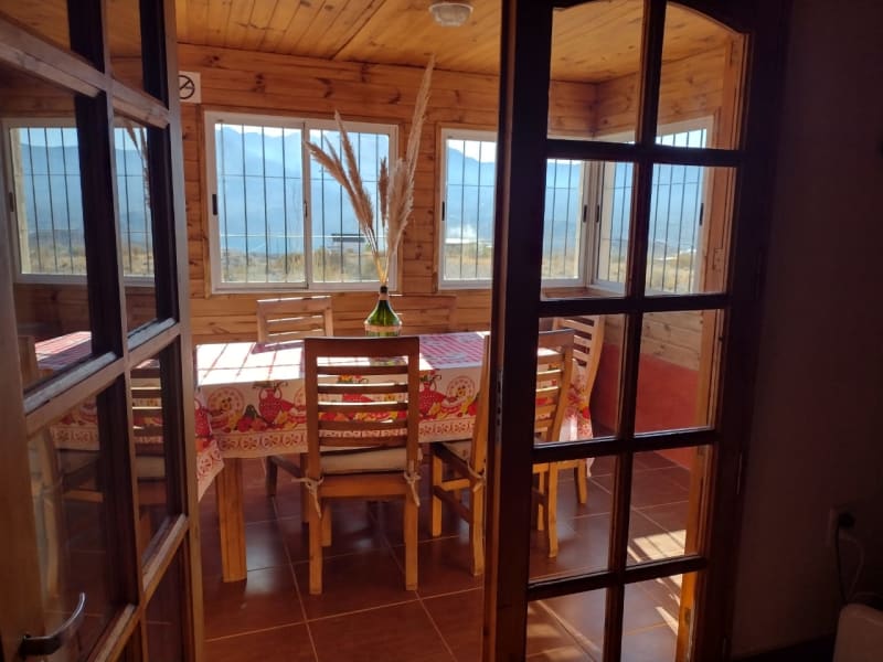 Vista hacia el comedor vidriado a través de puertas de madera con luz natural y paisaje serrano