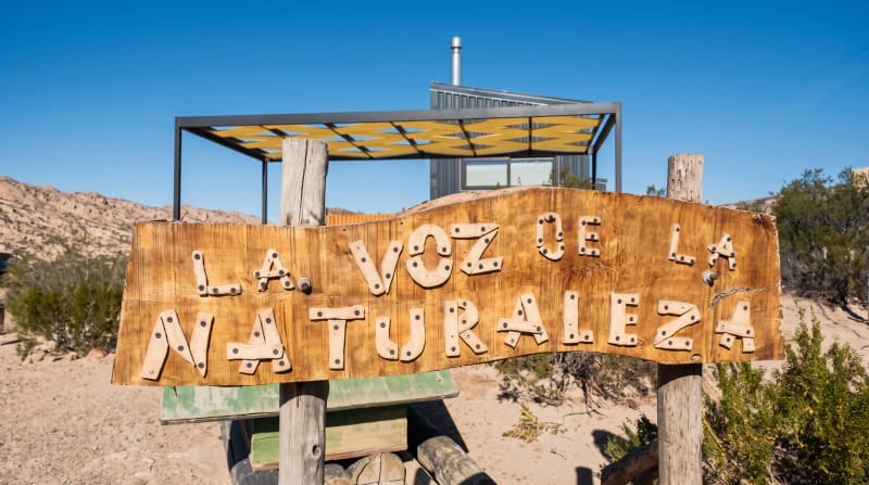 Cartel rústico de madera tallada con el nombre La Voz de La Naturaleza en el acceso al predio
