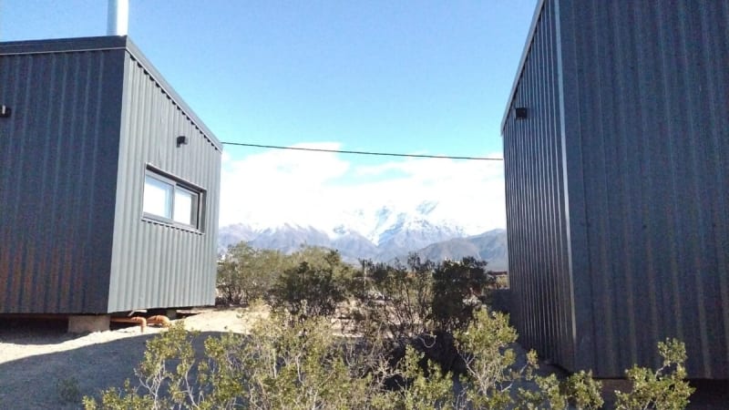 Vista entre las dos cabañas modulares enmarcando la vegetación autóctona y la cordillera nevada