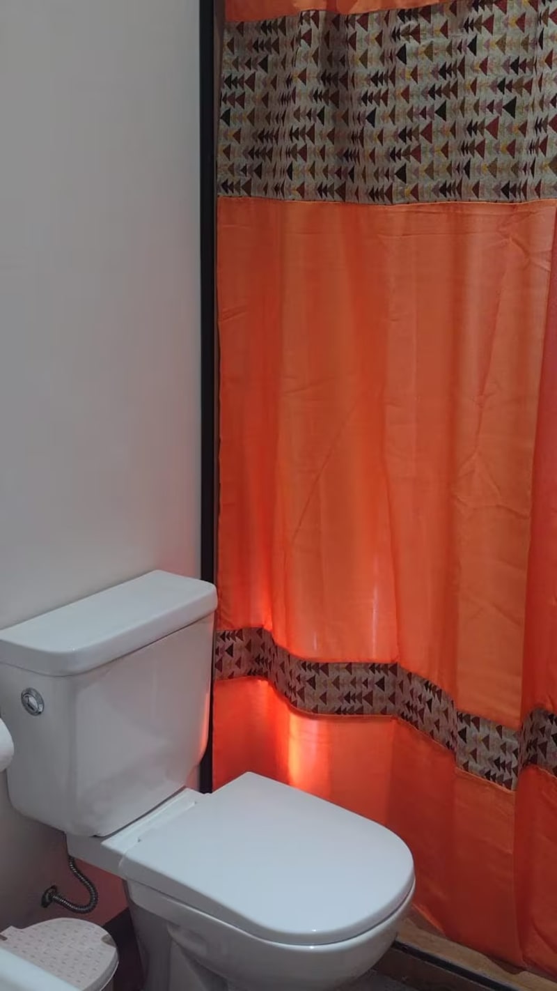 Sanitario con inodoro blanco y cortina de baño con guarda geométrica
