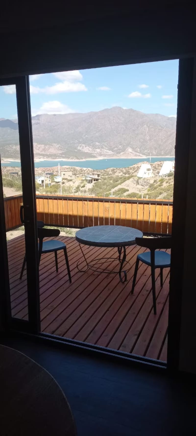 Mesa y sillas sobre el deck exterior de madera con vista abierta al embalse Potrerillos