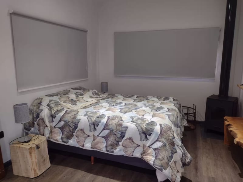 Dormitorio con cama matrimonial, mesas de noche de troncos naturales, cortinas roller y calefacción