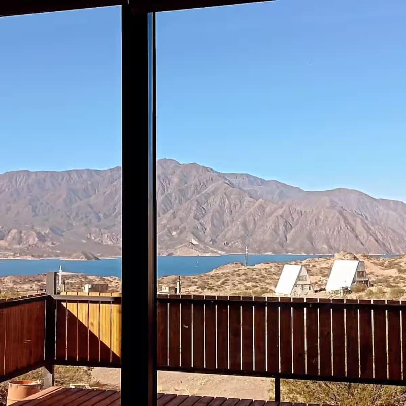 Perspectiva del deck de madera y el horizonte del lago Potrerillos con cabañas serranas a lo lejos