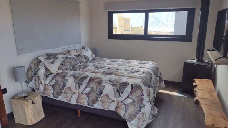 Dormitorio con cama somier de dos plazas, mesas de luz de tronco rústico y ventanal apaisado con vistas