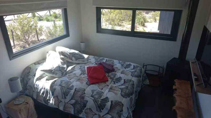 Cama matrimonial iluminada por el sol de mañana con toallas de baño preparadas y salamandra contigua
