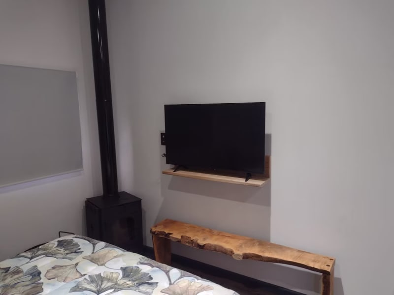 Smart TV sobre estante flotante y banco artesanal de madera maciza frente a la cama