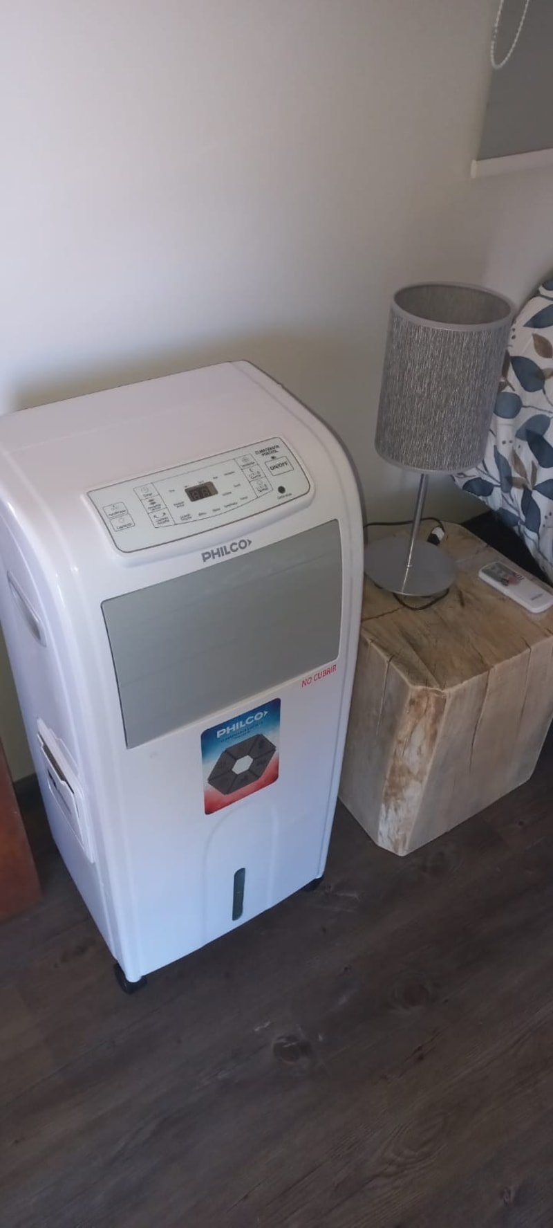 Climatizador portátil marca Philco con panel digital junto a la mesa de noche de madera