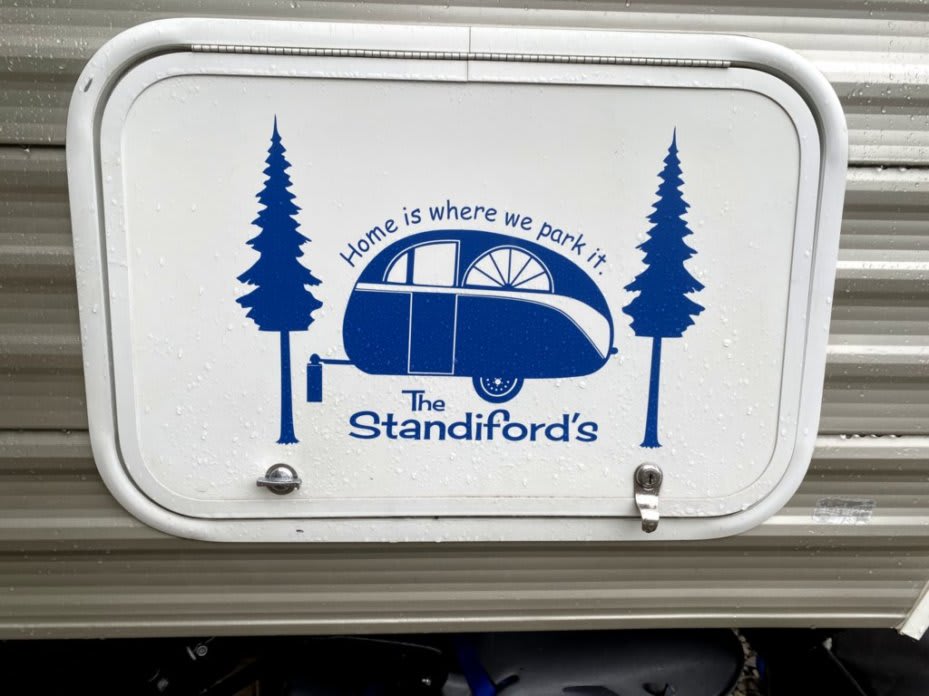 One of our storage doors with a sticker on it. The sticker is a picture of two pine trees, and a retro camper. The sticker reads &quot;The Standifords, Home is where you park it&quot;
