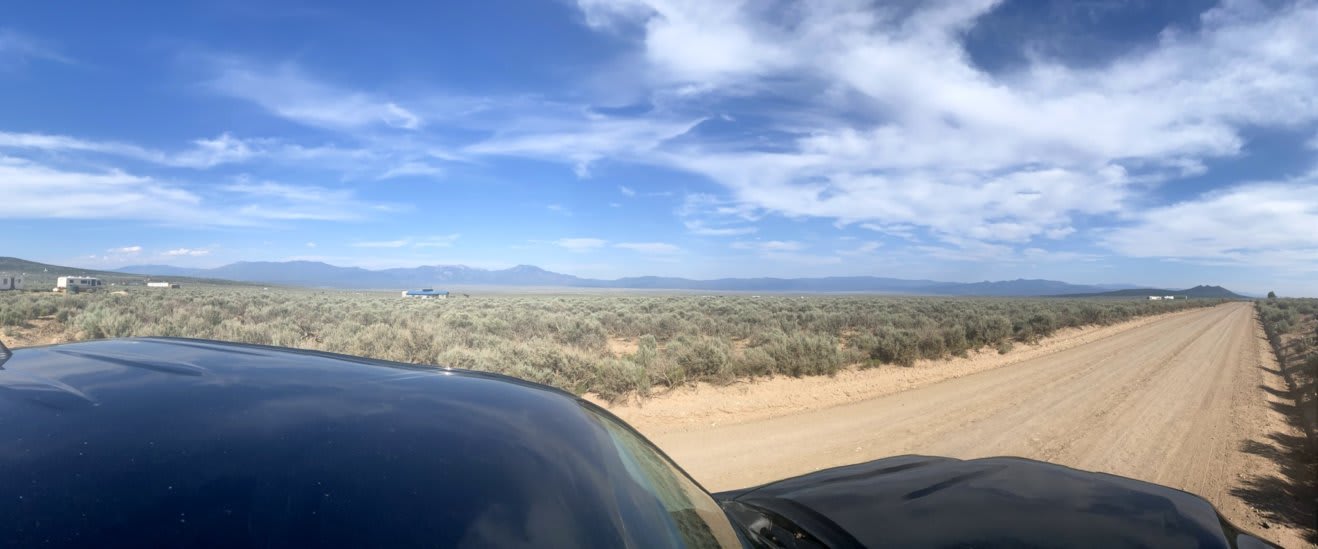 high desert landscape in panoramic orientation depicting mountains in the distance and sage brush on miles of visible land