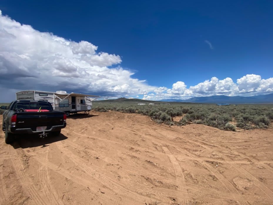 picture of a black truck parked behind a travel trailer with a dirt driveway in the foreground and a deep blue sky with huge fluffy white and blue-grey clouds on the left side stretching around to the right