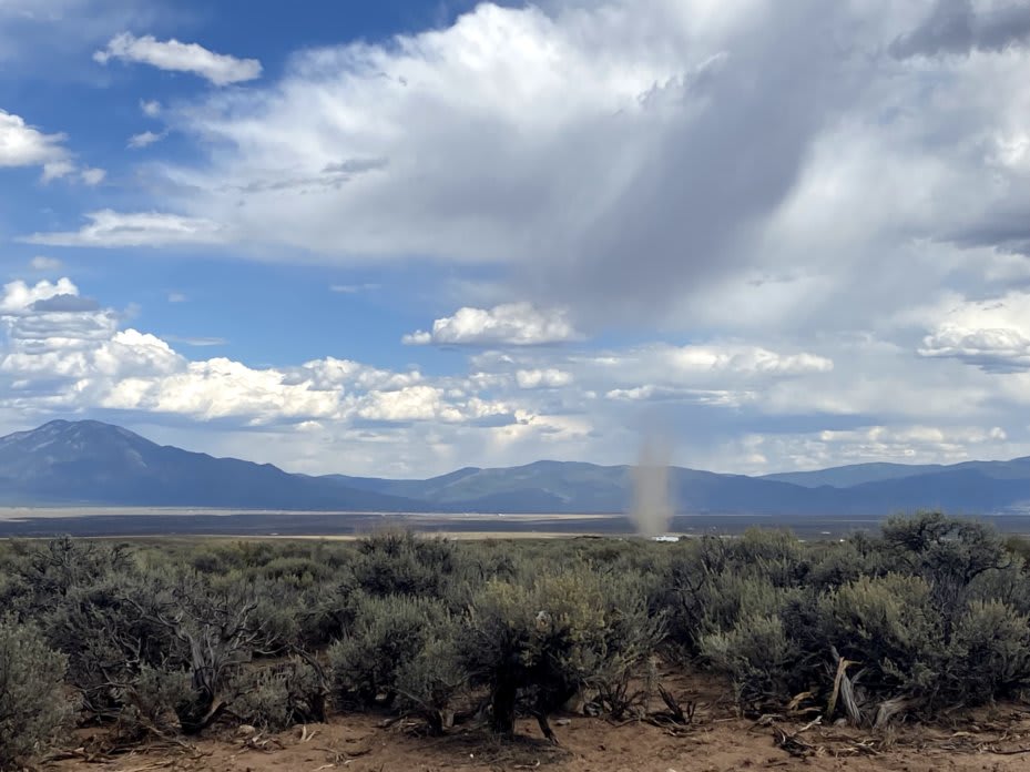 view of a sage covered mesa with mountains in the background and a large dust cyclone in the foreground