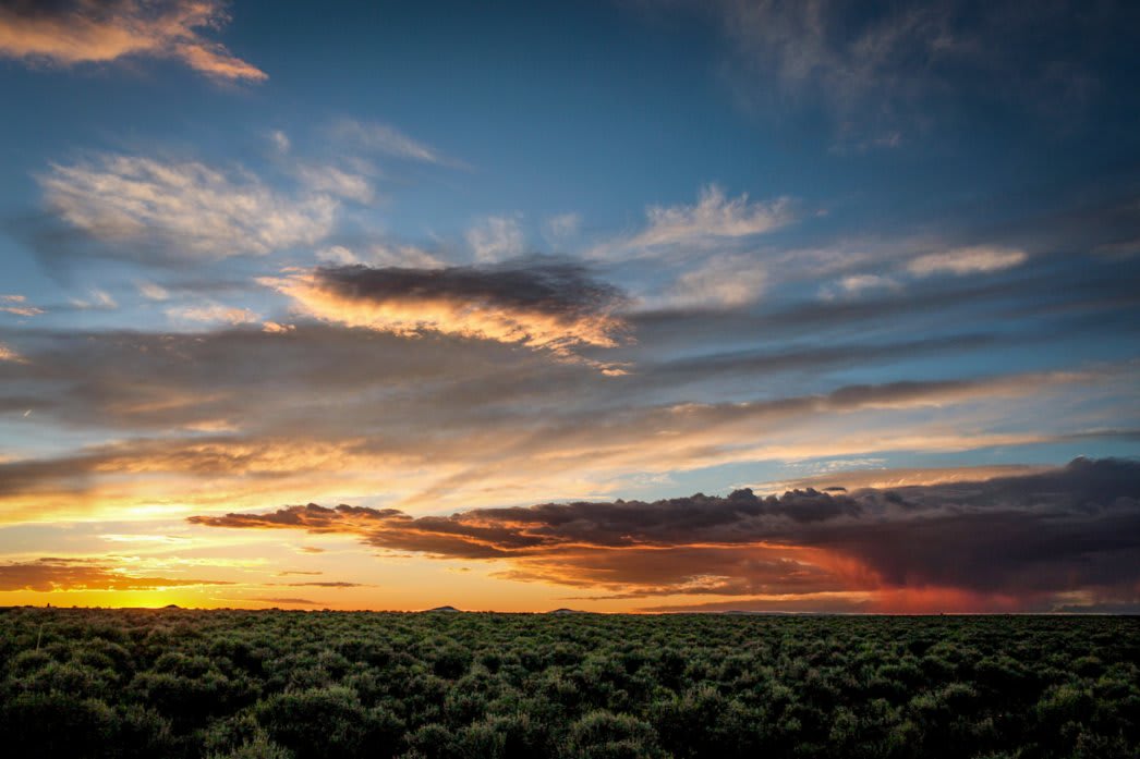 a beautiful sunset on a sage covered mesa with a low cluster of clouds and a visible downpouring of rain