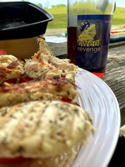 Outdoor closeup photo of some chicken, and a bottle of wine. They are resting on a picnic table.