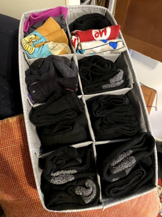 A bin containing neatly-folded socks. The bin has a divider that separates the socks into 8 compartments. Each compartment holds 2-3 pairs of socks.