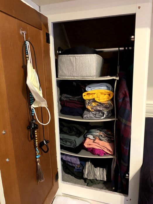 Kate's wardrobe. There is a hanging system that has three shelves. Each shelf has neatly folded articles of clothing. There is a bin on-top of the shelves that holds kate's unders.