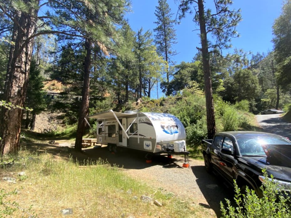 image of a travel trailer parked between trees on a sunny day with a black truck in the foreground