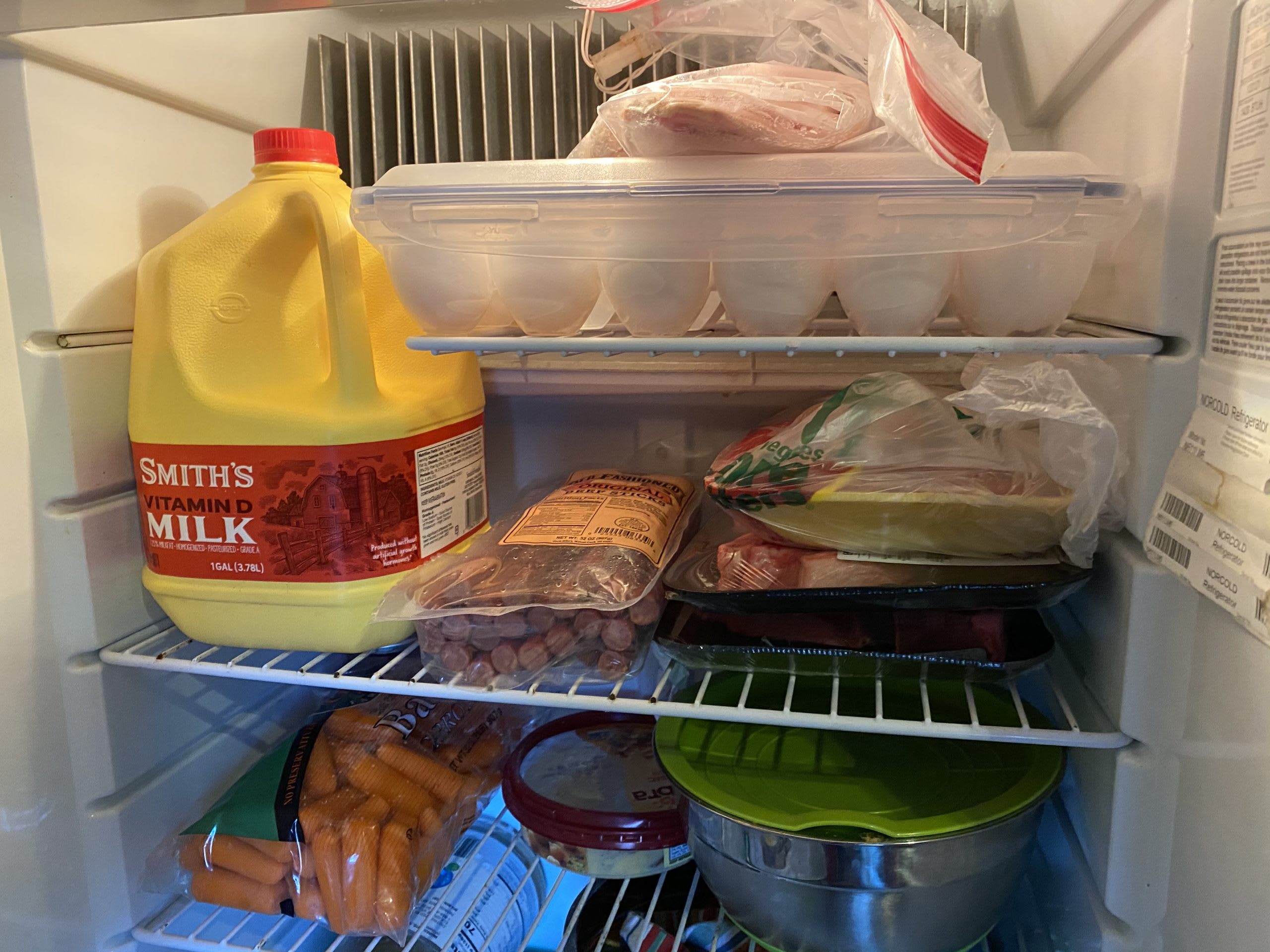 The top three shelves of our refrigerator. It is full of eggs, various meats, leftovers, milk, and carrots.