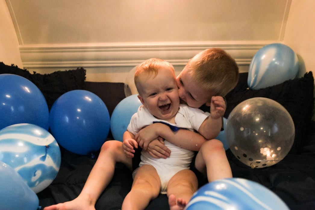 My two sons hugging and smiling on a bed surrounded by balloons from the youngest's first birthday celebration in our rv.