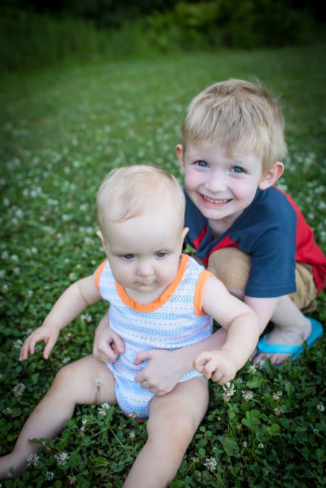 Outdoor portrait of our two sons, Bennett and Devin. Devin is 11 months old, and is being hugged from behind by his 5-year old brother, Bennett. Ben is looking at the camera and smiling.