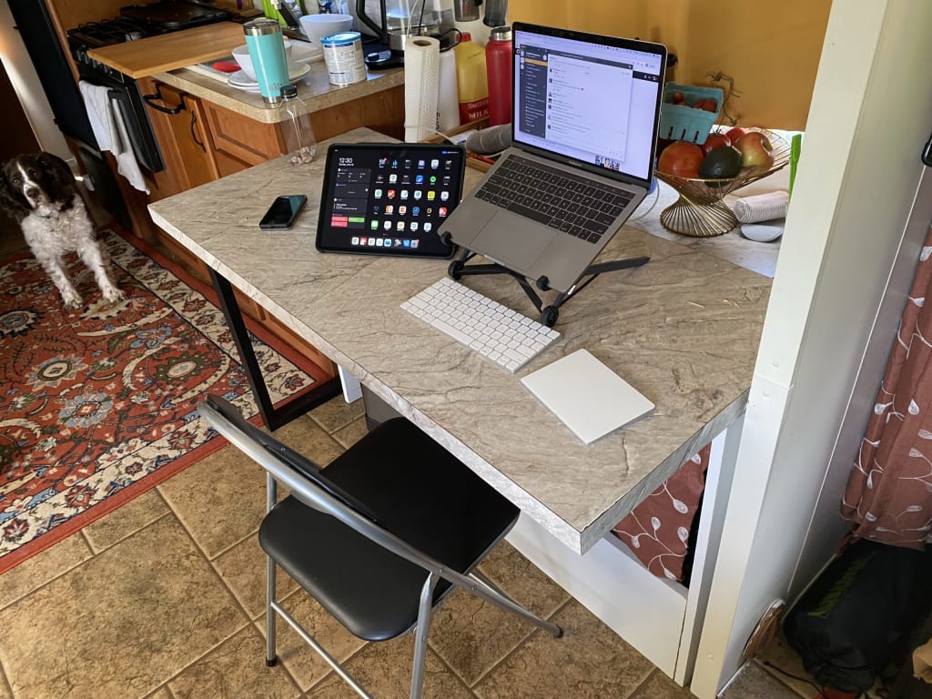 Alex's indoor work desk. You can see Alex's laptop, elevated by a Roost laptop stand, beside an iPad, mouse and keyboard.