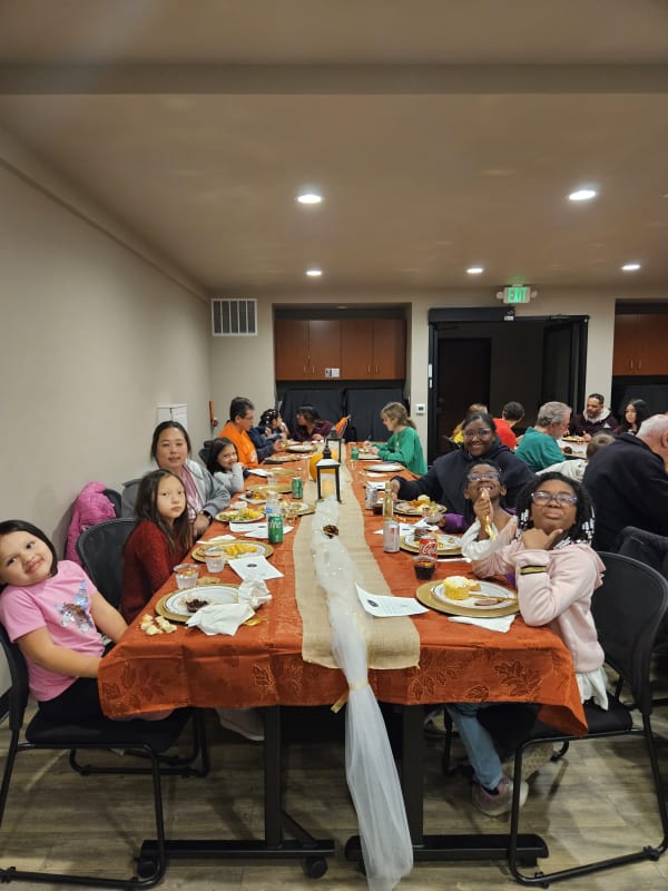 Families and children gathered at a long table for a community social dinner event at The Arc PPR